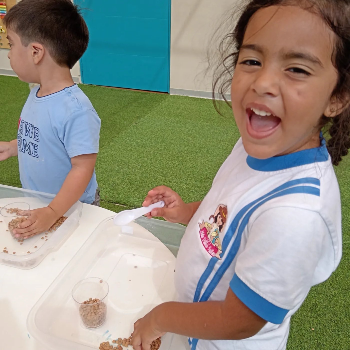 Niña sonriendo mientras trasvasa granos con una cuchara durante una actividad sensorial
