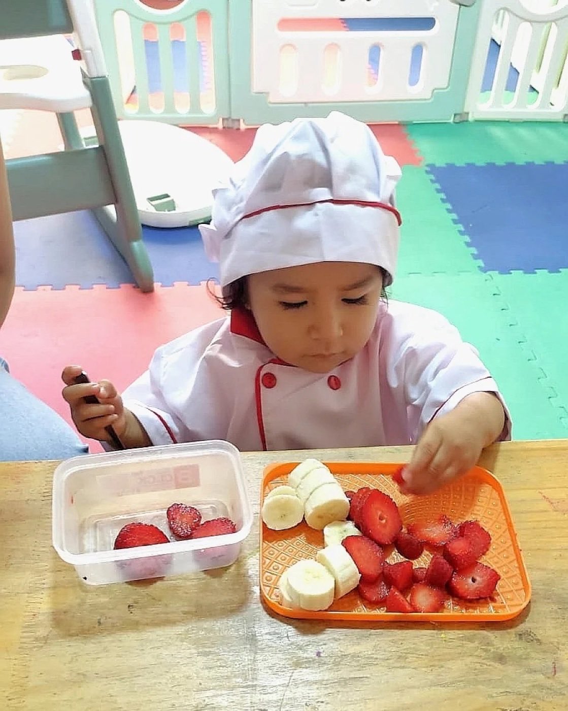 Niña con gorro y mandil de chef preparando una ensalada de frutas