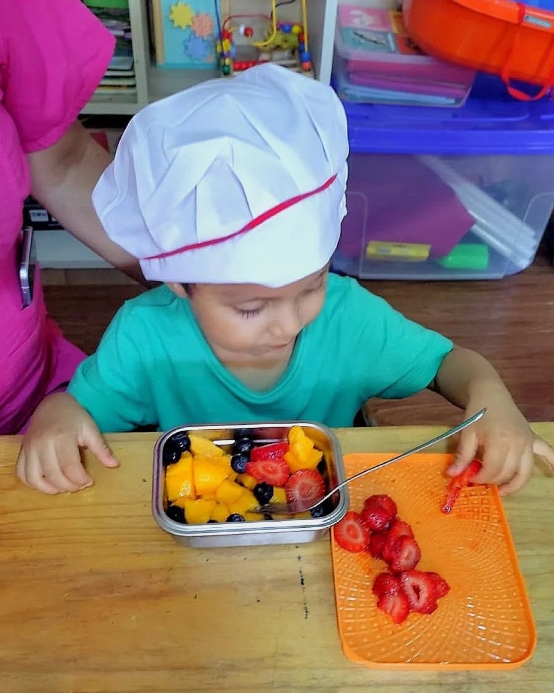 Niño con gorro de chef cortando fresas en el taller de cocina